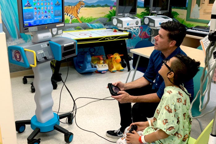 Adam Garone at a hospital sitting with a child in the hospital playing on a Nintendo Switch gaming station